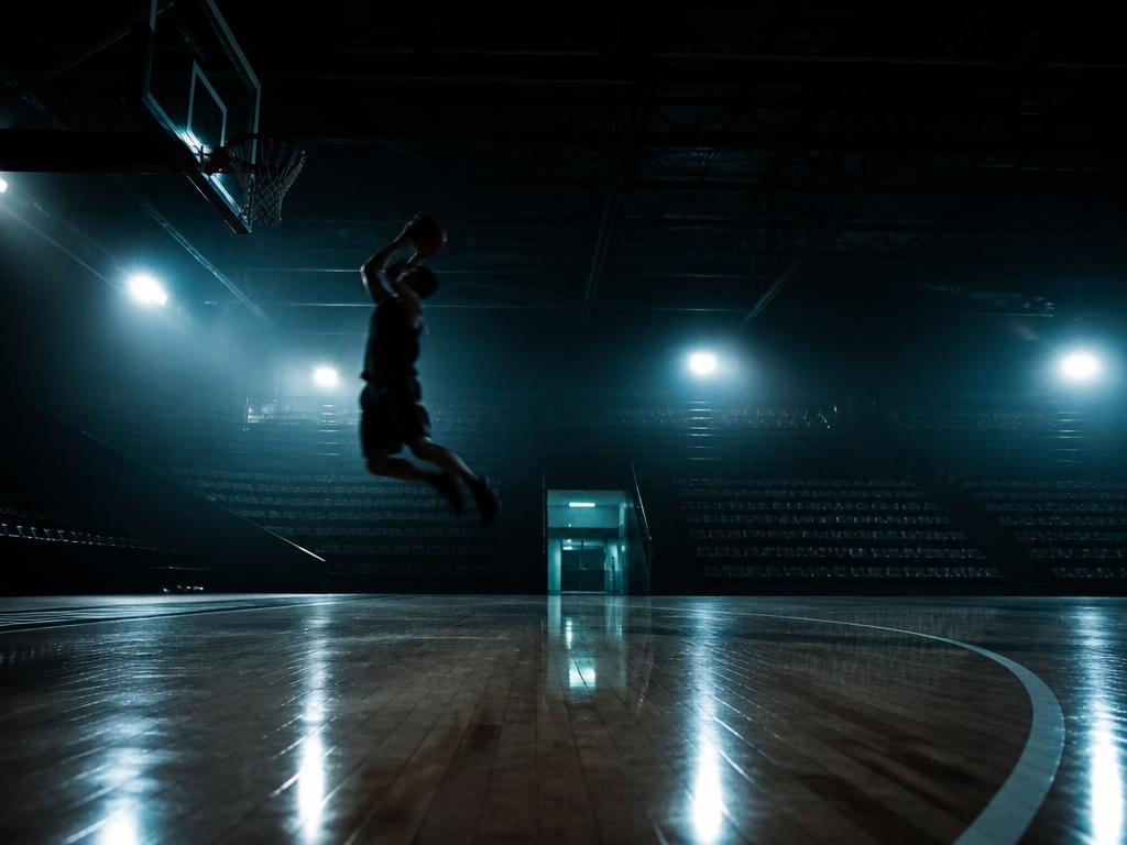 Mörk basketarena med en spelare i luften ovanför parketten